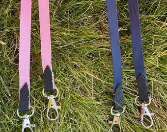 May include: Pink and navy blue dog leashes with silver-colored metal clasps and black leather accents. The leashes are made of a durable, woven material and are displayed on a bed of green grass.