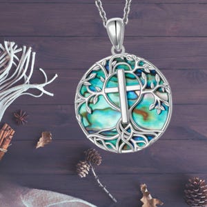 May include: A silver necklace with a round pendant featuring a silver tree of life design with a cross in the center. The pendant is made of abalone shell with iridescent blue, green, and brown colors.