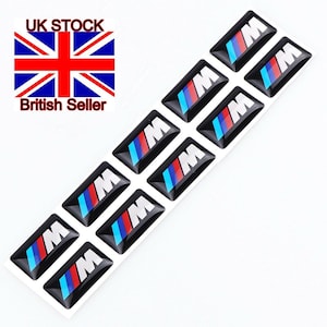 May include: Ten blue, red and white BMW logo stickers on a white background. The stickers are rectangular and have a glossy finish.