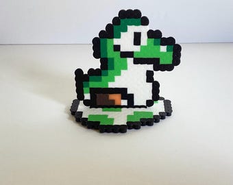 May include: A green and white Yoshi character from the Super Mario Bros. video game series, made with perler beads. The Yoshi is sitting on a green and white platform.