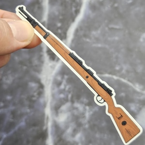 May include: A brown wooden rifle with a black metal barrel and a black metal scope. The rifle is a sticker.