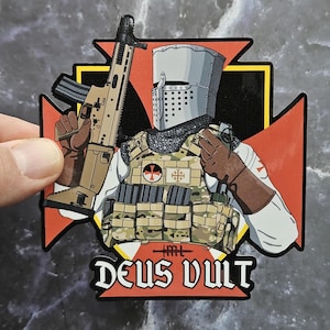 May include: A sticker featuring a cartoon illustration of a knight in a helmet and tactical vest, holding a rifle. The knight is set against a red and white cross design, with the words "DEUS VULT" at the bottom.