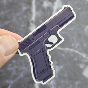 Puede incluir: Una pegatina troquelada con la ilustración de una pistola semiautomática de color gris oscuro. El diseño muestra el perfil lateral del arma de fuego con una empuñadura texturizada, un guardamonte y una corredera. Tiene un borde blanco.