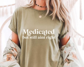 May include: A green t-shirt with the text "Medicated but still ain't right" printed in white.