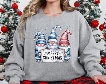 May include: A gray sweatshirt with a Christmas design featuring three gnomes holding a sign that says "Merry Christmas". The gnomes are wearing blue and red hats and have white beards. The sweatshirt is paired with red and black plaid pajama pants.