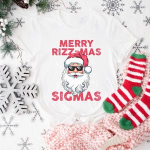 May include: White t-shirt with a red and white Santa Claus graphic and the text "Merry Rizzmas Sigmas".