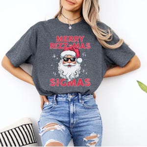 May include: A gray t-shirt with a red and white Santa Claus wearing sunglasses and the text "Merry Rizz-Mas Sigmas".