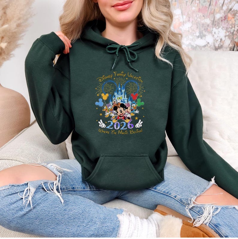 Peut inclure: Sweat-shirt &agrave; capuche vert fonc&eacute; avec un motif Disney Family Vacation. Le graphisme comprend des personnages Disney, un ch&acirc;teau, des feux d'artifice et l'ann&eacute;e 2026. Le texte "Where The Magic Begins" est &eacute;galement pr&eacute;sent. Le sweat-shirt a une poche avant et une capuche &agrave; cordon.
