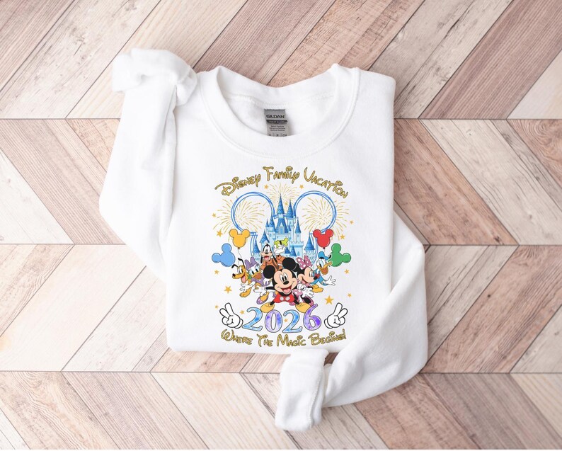 Peut inclure: Sweat-shirt blanc avec un graphisme color&eacute; repr&eacute;sentant des personnages Disney, un ch&acirc;teau et le texte "Disney Family Vacation 2026". Le motif comprend Mickey Mouse, Minnie Mouse, Donald Duck et Dingo. La phrase "Where The Magic Began" est &eacute;galement incluse.