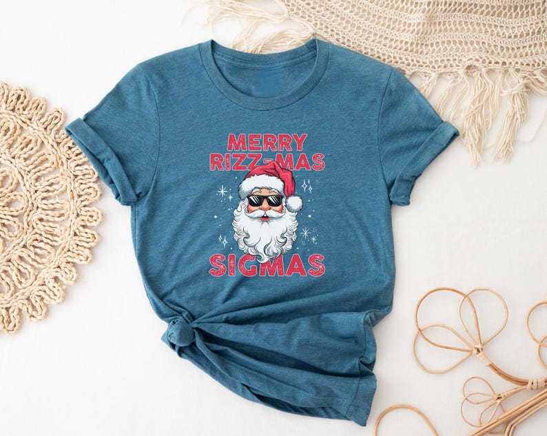 May include: A teal blue t-shirt with a graphic of Santa Claus wearing sunglasses and the text "Merry Rizzmas Sigmas".