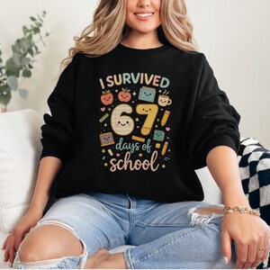 May include: Black sweatshirt with the text "I Survived 67 Days of School" in a colorful, playful design. The graphic includes smiling numbers, apples, books, and pencils, perfect for teachers or students.