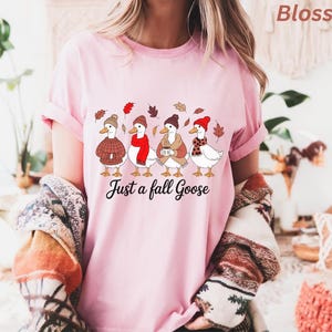 May include: Pink t-shirt with a graphic of four geese wearing fall attire, including hats and scarves, with the text "Just a fall Goose". The geese are surrounded by fall leaves.