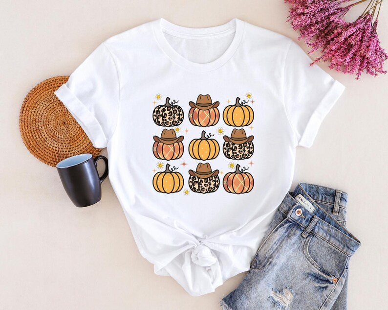 Puede incluir: Camiseta blanca con un gr&aacute;fico de varias calabazas con sombreros de vaquero. Las calabazas son de color naranja y marr&oacute;n con un dise&ntilde;o de estampado de leopardo.