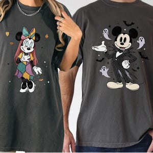 May include: Two dark gray t-shirts featuring Disney characters. One shirt displays Minnie Mouse in a patchwork dress, the other shows Mickey Mouse dressed as Jack Skellington, surrounded by ghosts and bats. Both shirts have a vintage, distressed look.