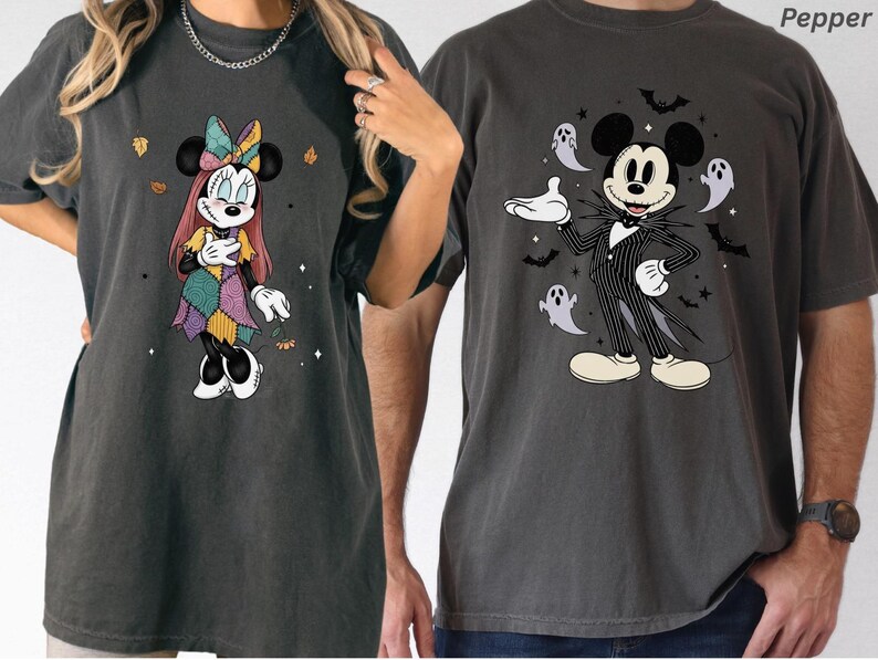 May include: Two dark gray t-shirts featuring Disney characters. One shirt displays Minnie Mouse in a patchwork dress, the other shows Mickey Mouse dressed as Jack Skellington, surrounded by ghosts and bats. Both shirts have a vintage, distressed look.