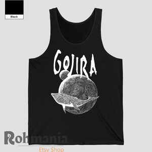 May include: Black tank top featuring the word "GOJIRA" in white script above a detailed white illustration of a whale swimming around a planet with a swirling design. The tank top is a solid black color.