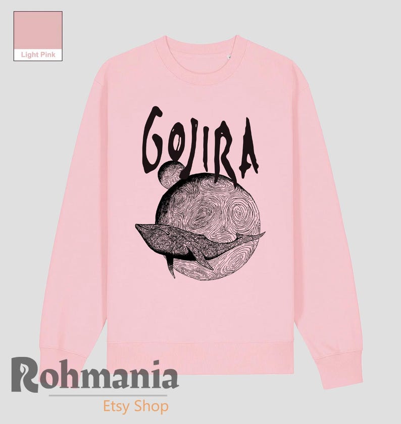 May include: Light pink sweatshirt with a black graphic. The graphic features the word "GOJIRA" above a detailed illustration of a whale swimming in front of a planet-like design. The Etsy shop name "Rohmania" is at the bottom.