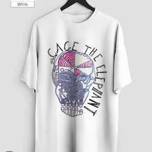 May include: White t-shirt with a graphic skull design. The skull is divided into sections with various patterns and colors, including pink, blue, and white. The text "CAGE THE ELEPHANT" is printed around the skull. The shirt is hanging on a black hanger.