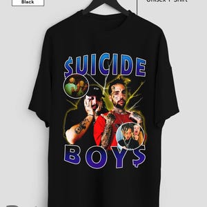 May include: Black unisex t-shirt with the words "SUICIDE BOYS" in blue and white, and images of two people. The shirt has a crew neck and short sleeves. The text "Unisex T-Shirt" is printed on the top right.