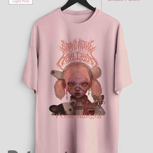 以下が含まれることがあります： ピンク色のユニセックスTシャツ。ピンクの髪と銃のようなオブジェクトを持つ人形のような人物のグラフィックが特徴です。「BRING ME YOUR EGO」と「POST HUMAN」の文字がプリントされています。Etsyショップ名「Rohmania」が下にあります。