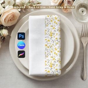 Puede incluir: Una servilleta de tela blanca doblada con un estampado floral amarillo en un lado, colocada sobre un plato blanco. La servilleta forma parte de un servicio de mesa, con un tenedor y un vaso visibles. El texto "Mockup • Easy to Use • Just Drag & Drop" está arriba.