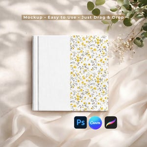 May include: A white book with a floral pattern of yellow flowers and green leaves on the right side. The text "Mockup • Easy to Use • Just Drag & Drop" is at the top. The book is on a white fabric surface.