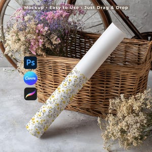 May include: A white cylindrical tube featuring a repeating pattern of small yellow flowers and green leaves. The tube is positioned diagonally in front of a woven wicker basket containing dried pink, purple, and white flowers.