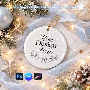 Könnte beinhalten: Ein rundes weißes Keramikornament mit dem schwarzen Text Your DESIGN Here sowie einer kleinen Schleifen- und Blattgrafik. Das Ornament hat eine goldene Aufhängeschnur und ist zwischen festlichen Dekorationen und Lichtern platziert.