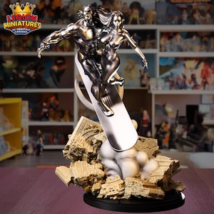 Könnte beinhalten: Eine silberfarbene Statue von zwei Figuren, die auf einem Surfbrett über einer zerbröckelnden Struktur reiten. Die Statue hat einen schwarzen Sockel. Das Logo "LEGION MINIATURES 3D PRINTING DESIGNS" ist sichtbar.