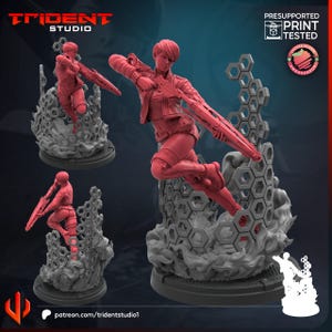 May include: A red 3D-printed figurine of a woman in a dynamic pose, holding a rifle. The figure is mounted on a gray base with a stylized cloud and honeycomb design. The Trident Studio logo and "Presupported Print Tested" text are visible.