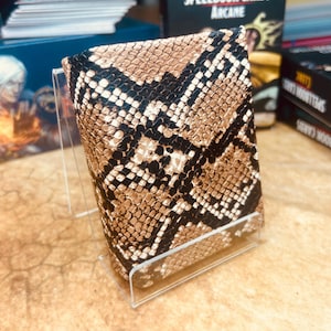 May include: A brown and black snakeskin-patterned card deck box. The box is made of a soft, textured material and is designed to hold a standard deck of playing cards.