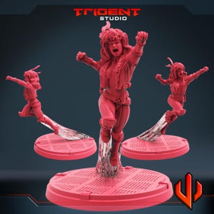May include: A red figurine of a woman in a dynamic pose, with arms raised and a determined expression. The figure is on a circular base, with two smaller versions on either side. The Trident Studio logo is at the top.