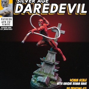 May include: A 40mm scale miniature figure of Daredevil in a red suit, posed dynamically on a weathered stone tombstone base with a cross. The figure holds a white billy club weapon. Text includes C27 STUDIO, SILVER AGE DAREDEVIL, and 40MM SCALE.