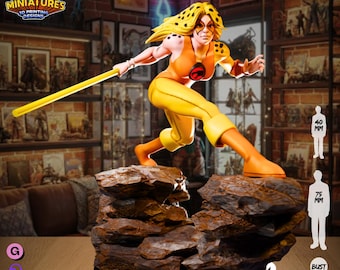 May include: A yellow and orange figurine of a female superhero, holding a yellow staff, stands on a rocky base. The figure is approximately 75 mm tall. The text "NOW INCLUDED IN 3 FORMATS" is visible. The Legion Miniatures logo is in the upper left corner.