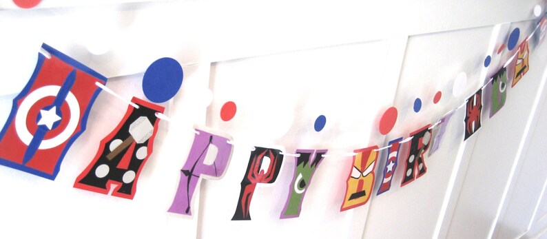 Pu&ograve; includere: Uno striscione di buon compleanno colorato con personaggi di supereroi. Le lettere sono decorate con immagini di Capitan America, Thor, Iron Man, Spider-Man, Hulk e un motivo a pois bianco e nero.