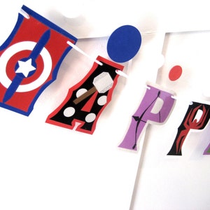 Pu&ograve; includere: Uno striscione colorato con la parola "HAPPY" scritta in diversi colori e design. Ogni lettera &egrave; decorata con un diverso tema di supereroi, tra cui Captain America, Thor, Iron Man e Spider-Man.