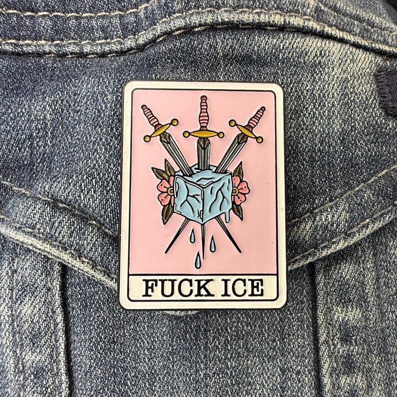 May include: A rectangular enamel pin with a light pink background featuring a central light blue ice cube pierced by three silver daggers with gold hilts, surrounded by small pink flowers and green leaves, with the text FUCK ICE in black letters.