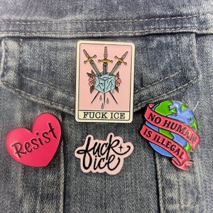 May include: Four enamel pins: a rectangular card with three swords piercing an ice cube and the text FUCK ICE, a heart-shaped pink pin with the word Resist, a pink script pin reading fuck ice, and a globe pin with a banner stating NO HUMAN IS ILLEGAL.