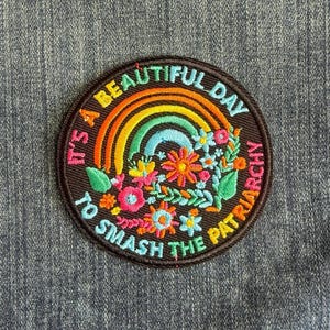 May include: Embroidered patch with a rainbow, flowers, and the text "It's a beautiful day to smash the patriarchy" in a circular design. The patch features orange, yellow, green, blue, and pink colors on a black background.