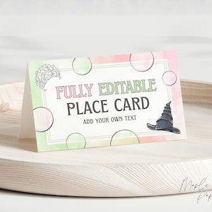 Könnte beinhalten: Eine gefaltete Platzkarte mit dem Text "FULLY EDITABLE PLACE CARD ADD YOUR OWN TEXT". Die Karte hat ein Aquarelldesign mit grünen und rosa Farbtönen sowie Illustrationen einer Tiara und eines Zaubererhuts.