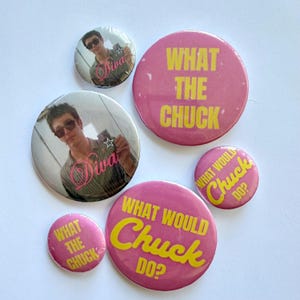 May include: A collection of six circular pin-back buttons. Two buttons feature a photograph of a person wearing sunglasses with the word Diva in pink script. Four buttons are pink with yellow text reading What The Chuck or What Would Chuck Do.