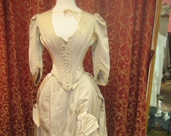 May include: A vintage ivory-colored wedding dress with a fitted bodice and a long train. The dress features a lace-up corset and a gathered skirt.