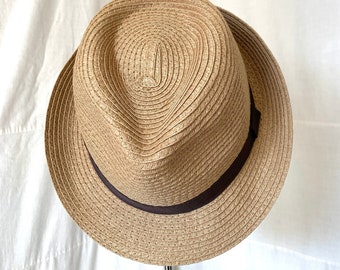 May include: A tan straw fedora hat with a brown ribbon band. The hat is on a stand.
