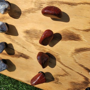 Pu&ograve; includere: Un pannello di legno con una finitura bruciata, che mostra una variet&agrave; di pomelli in pietra rossa e grigia. Il pannello ha la parola "Knobs" incisa su di esso.