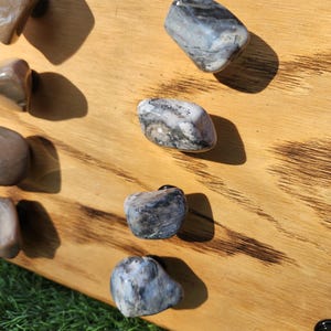 Pu&ograve; includere: Primo piano di sei pomelli in pietra naturale, ognuno con un motivo e un colore unici, montati su una tavola di legno. I pomelli sono di colore grigio chiaro con striature nere e bianche.