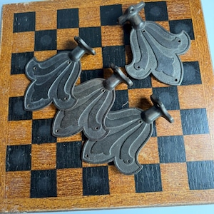 May include: Three dark grey metal hardware pieces with a fan-like shape and a small circular mounting base at the top. Each piece features a textured surface with raised lines and three small holes for screws, arranged in a symmetrical pattern.