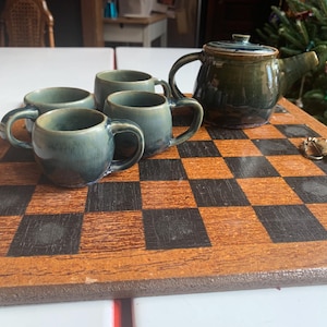 May include: A set of four teal green ceramic teacups and a matching teapot on a wooden checkerboard surface.