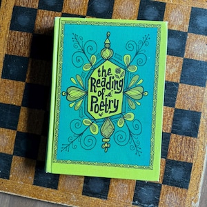 May include: A hardcover book titled "The Reading of Poetry" with a teal cover featuring ornate green and yellow designs. The book is set against a brown and black checkered background.