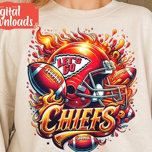 Op de afbeelding: Een wit sweatshirt met een grafisch ontwerp van een voetbalhelm met vlammen en de woorden "Let's Go Chiefs" in een gestileerd lettertype.