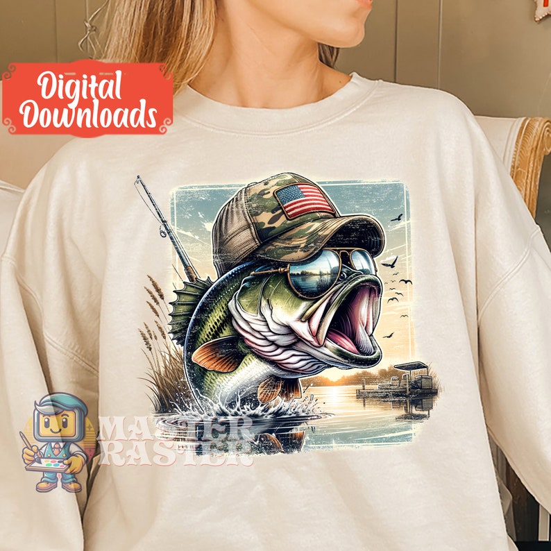 Op de afbeelding: Beige sweatshirt met een afbeelding van een largemouth bass met een zonnebril en een camouflage hoed met een Amerikaanse vlag. Het ontwerp bevat een hengel, water en een zonsondergang. De woorden "Digital Downloads" staan in een rode doos.